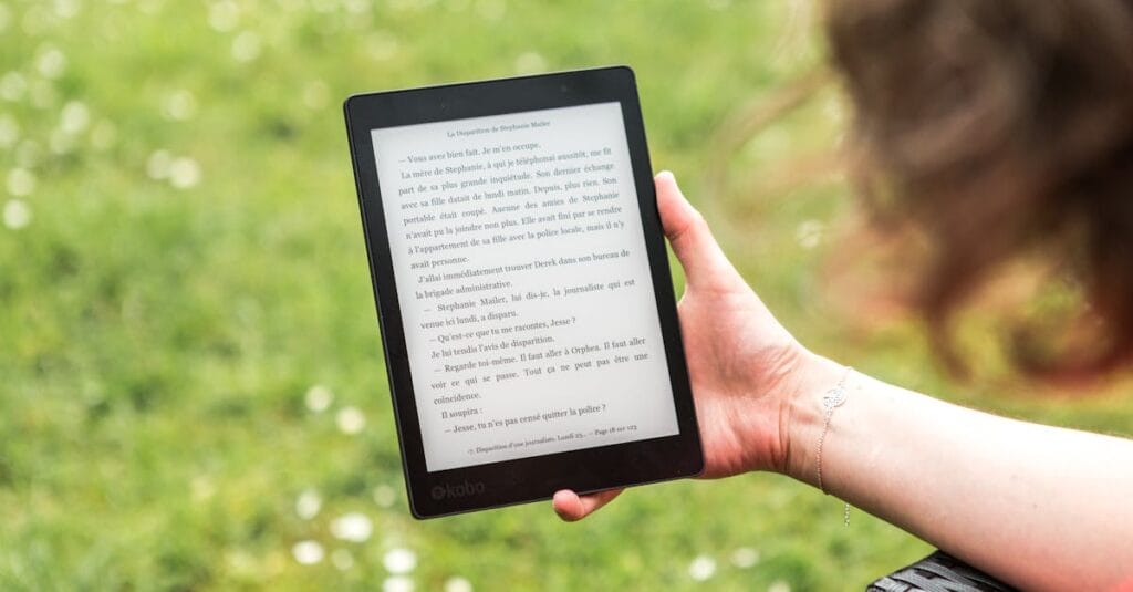 A person reads an eBook on a Kobo device while relaxing outdoors in a sunny park.